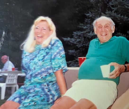Two friends share laughter while relaxing on a couch at a summer gathering outdoors.