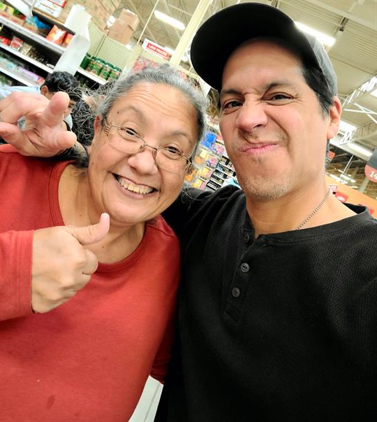 Two people share a happy moment, smiling and posing with thumbs up in a grocery store.