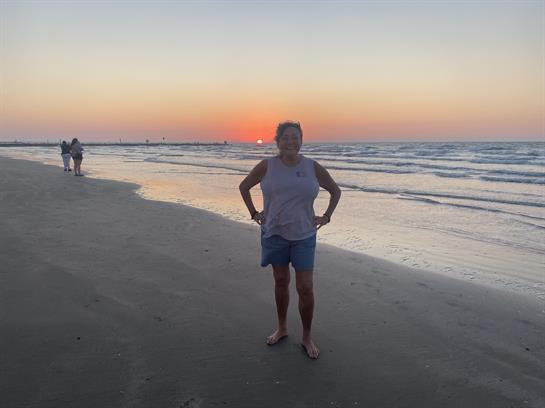 A person enjoys the beach as the sun sets, creating a vibrant horizon and calm waves.