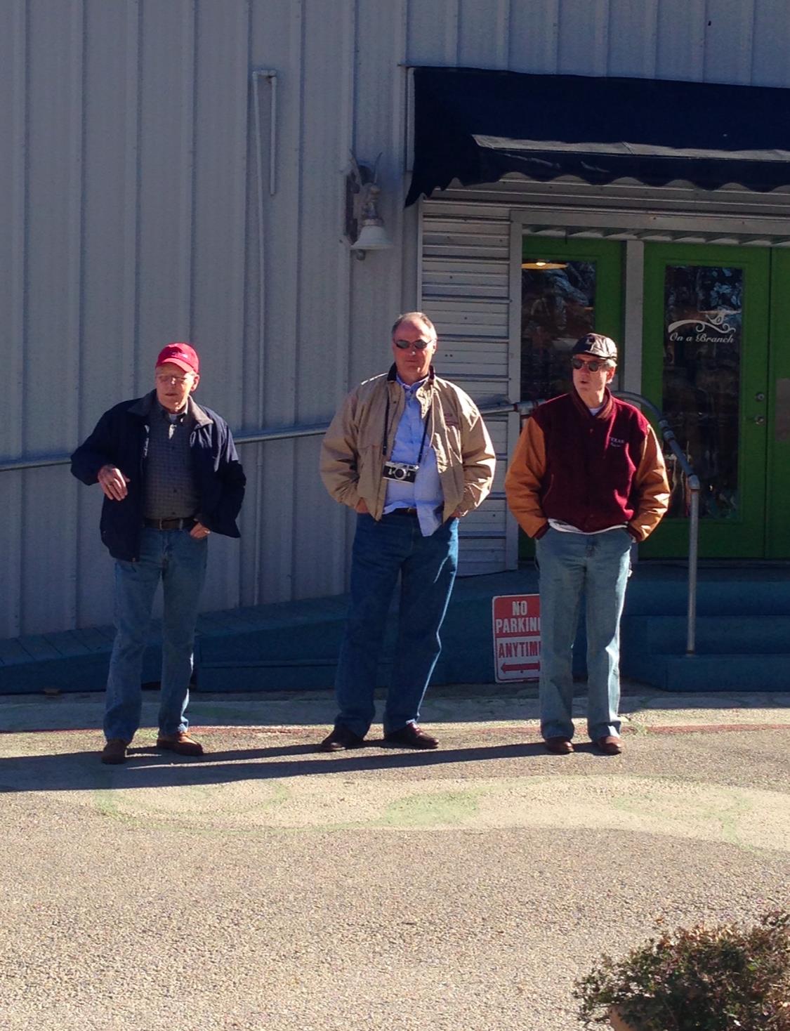 Three men engage in conversation outside a building on a clear day.