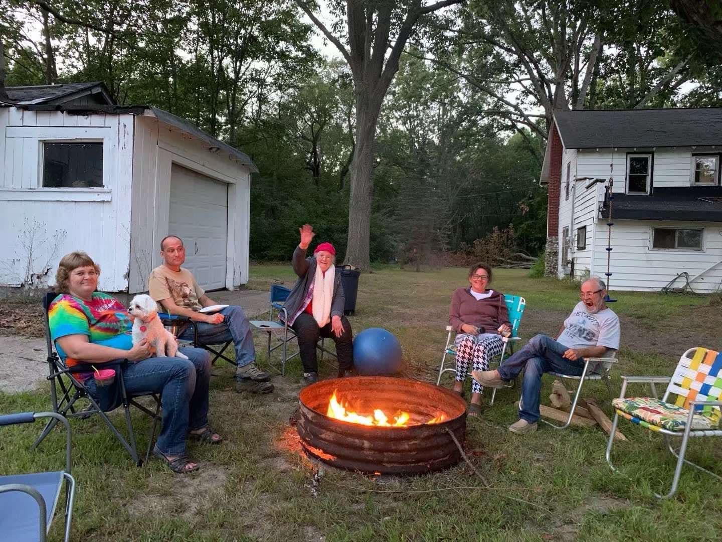 Group of friends enjoying a campfire while sitting in chairs during a cozy evening.