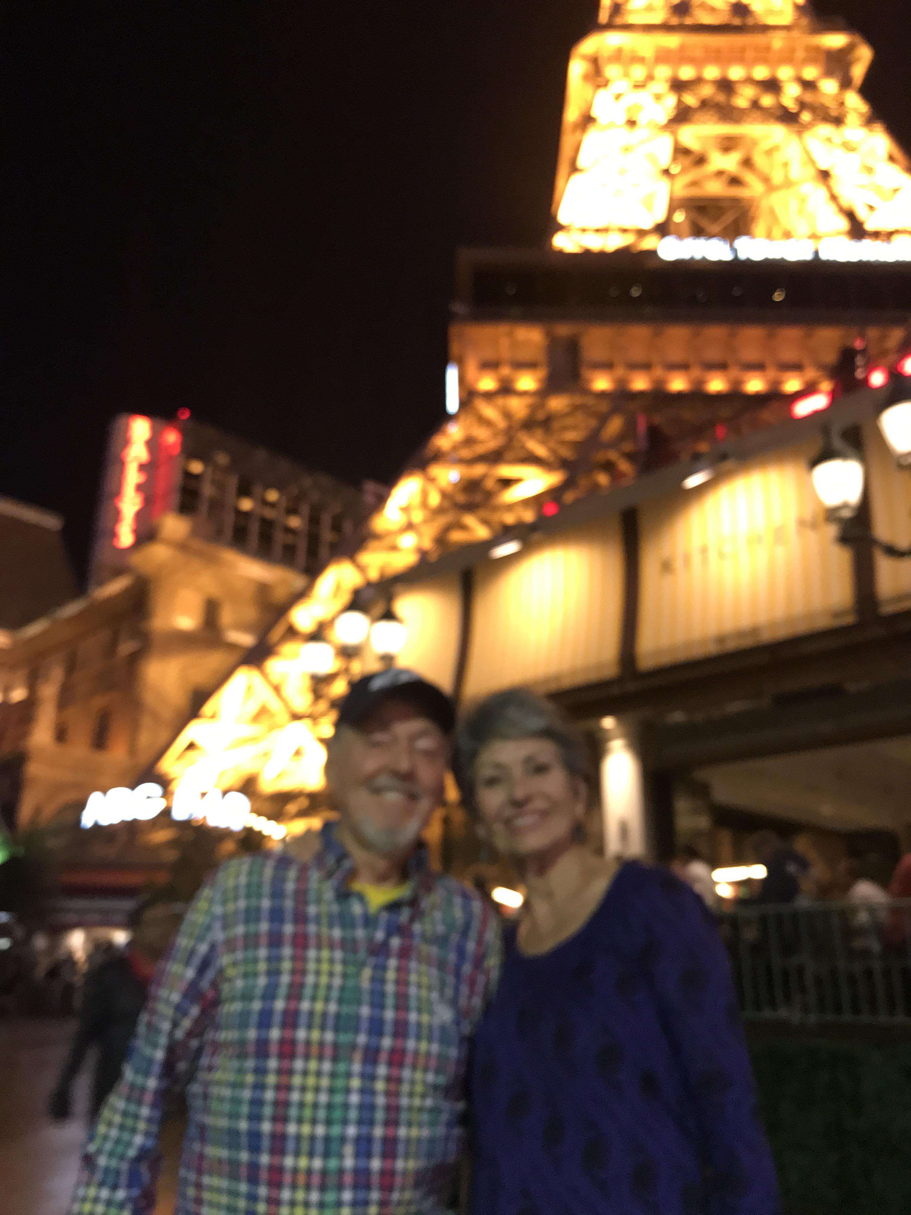 A happy couple poses by a famous landmark lit up at night, amid lively surroundings.