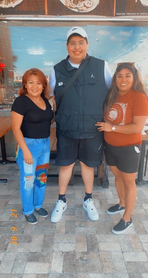 Three friends stand together outside a restaurant, smiling and enjoying the sunny weather.