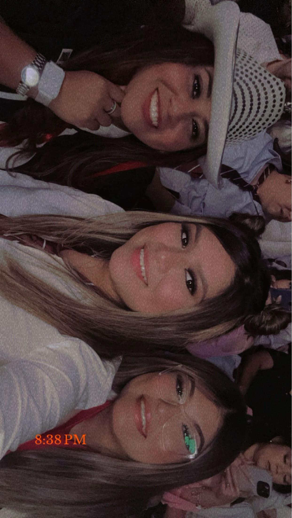 Three young women enjoy a fun moment while attending a lively event outdoors in the evening.