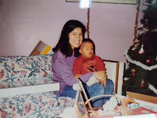 Woman sits on couch with baby in her arms, joyful atmosphere during home celebration season.