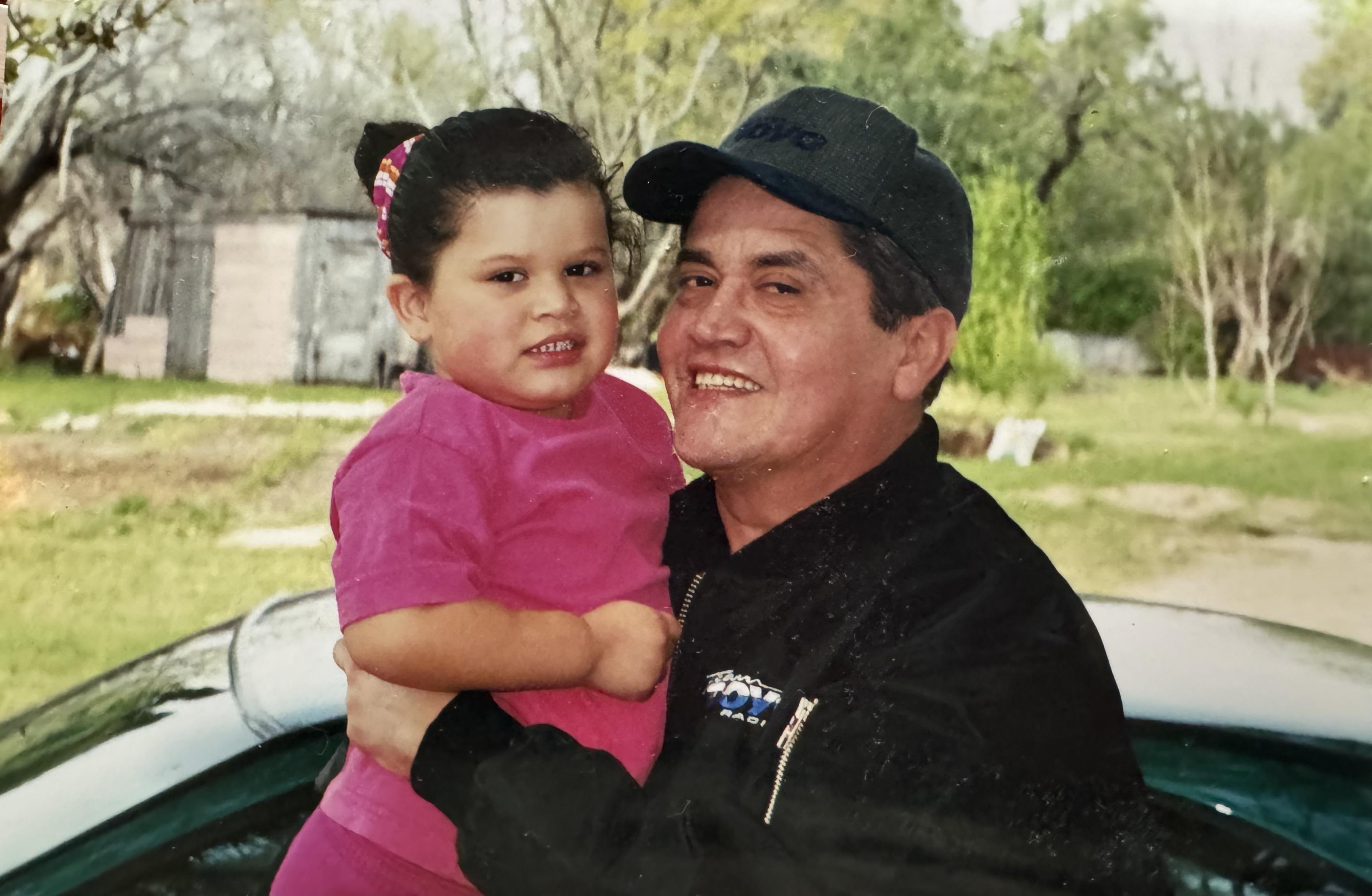 A man joyfully holds a young girl in a vibrant outdoor setting, both smiling.