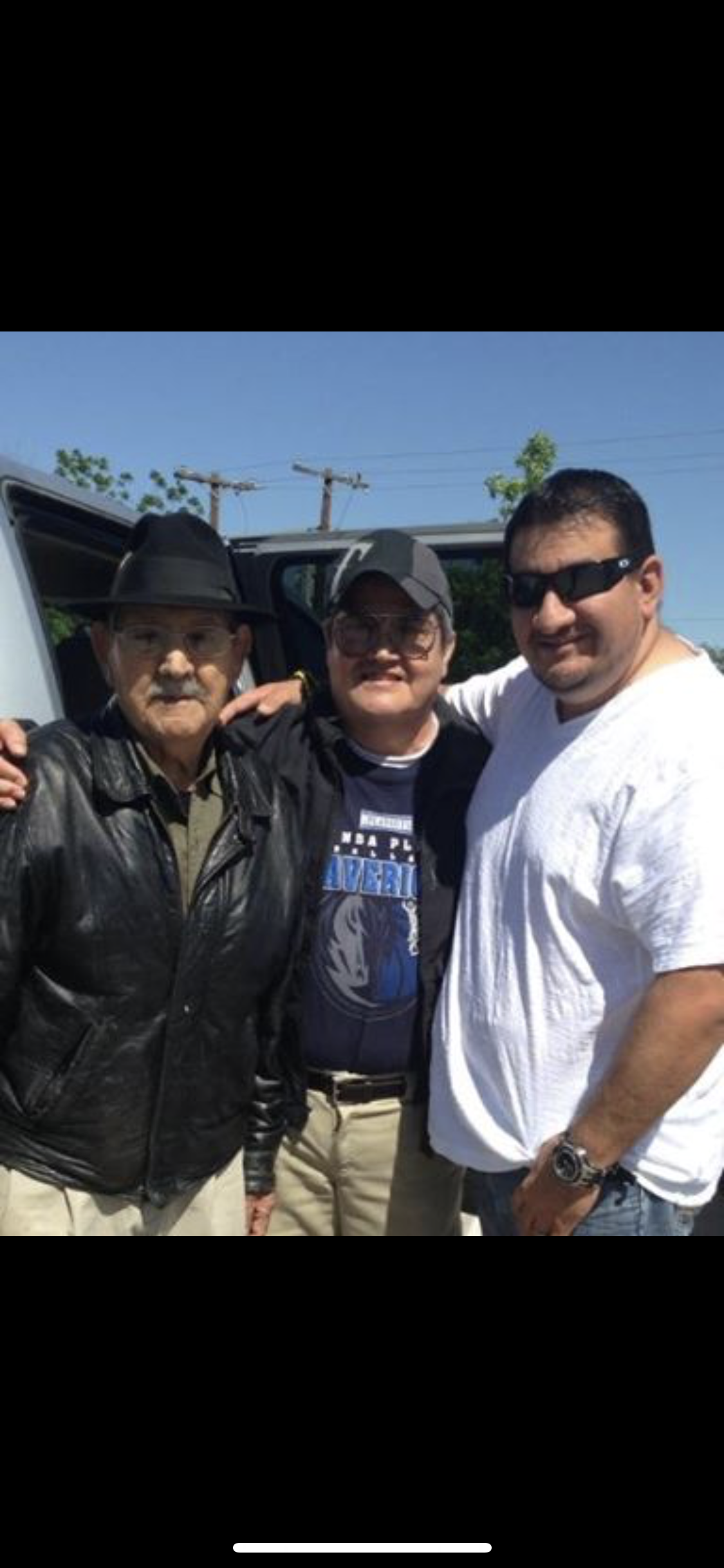 Three men pose together outdoors, smiling and enjoying a sunny day near a vehicle.
