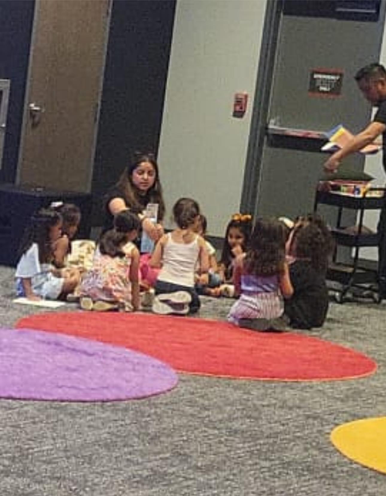 A group of young children sits together on colorful mats, focusing on a learning activity.