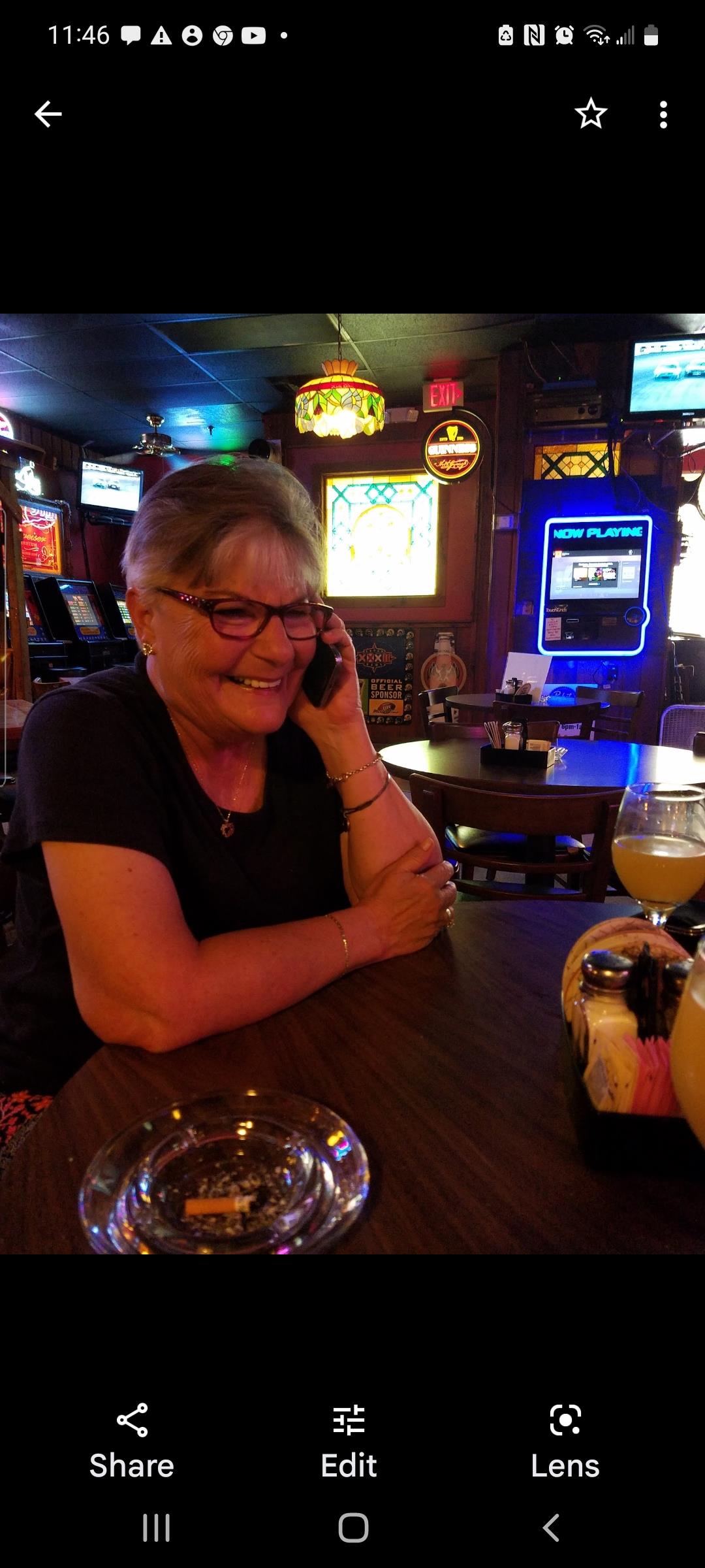 A woman with glasses smiles while chatting on the phone at a bar with colorful decor.