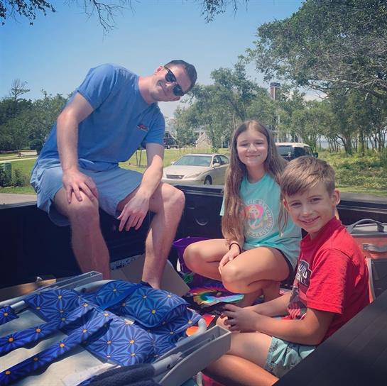 Children smile and play with toys while sitting in the back of a pickup truck on a sunny day.