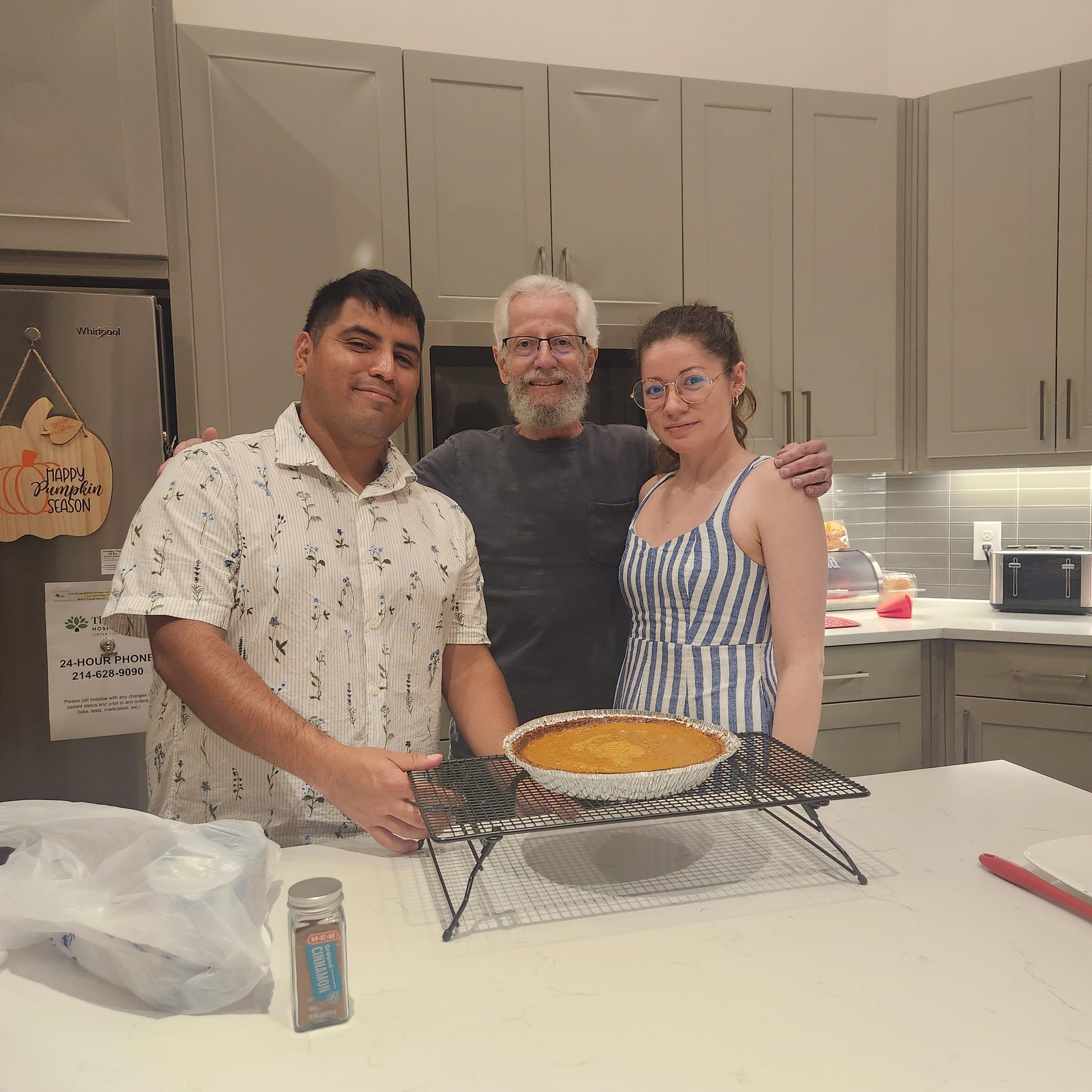 Three people share a brightly lit kitchen, showcasing a freshly baked dessert on the counter.