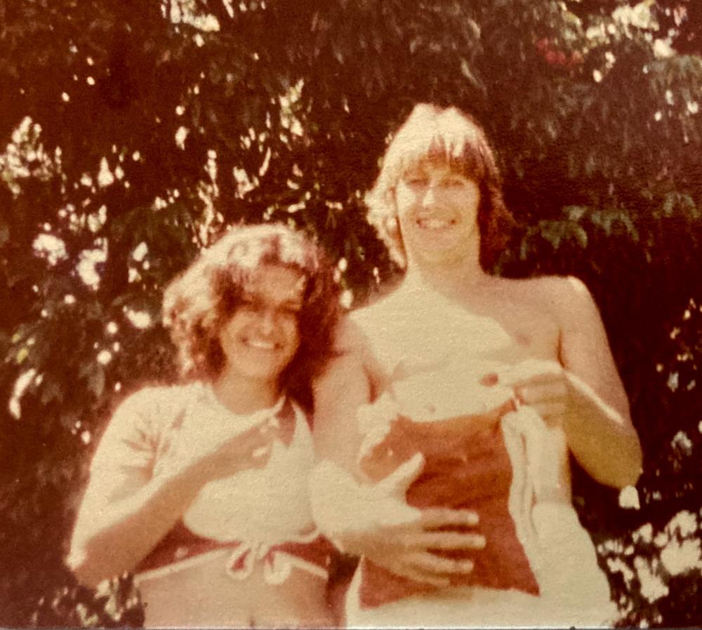 Friends are enjoying a sunny day in a garden, smiling while holding a pet together.