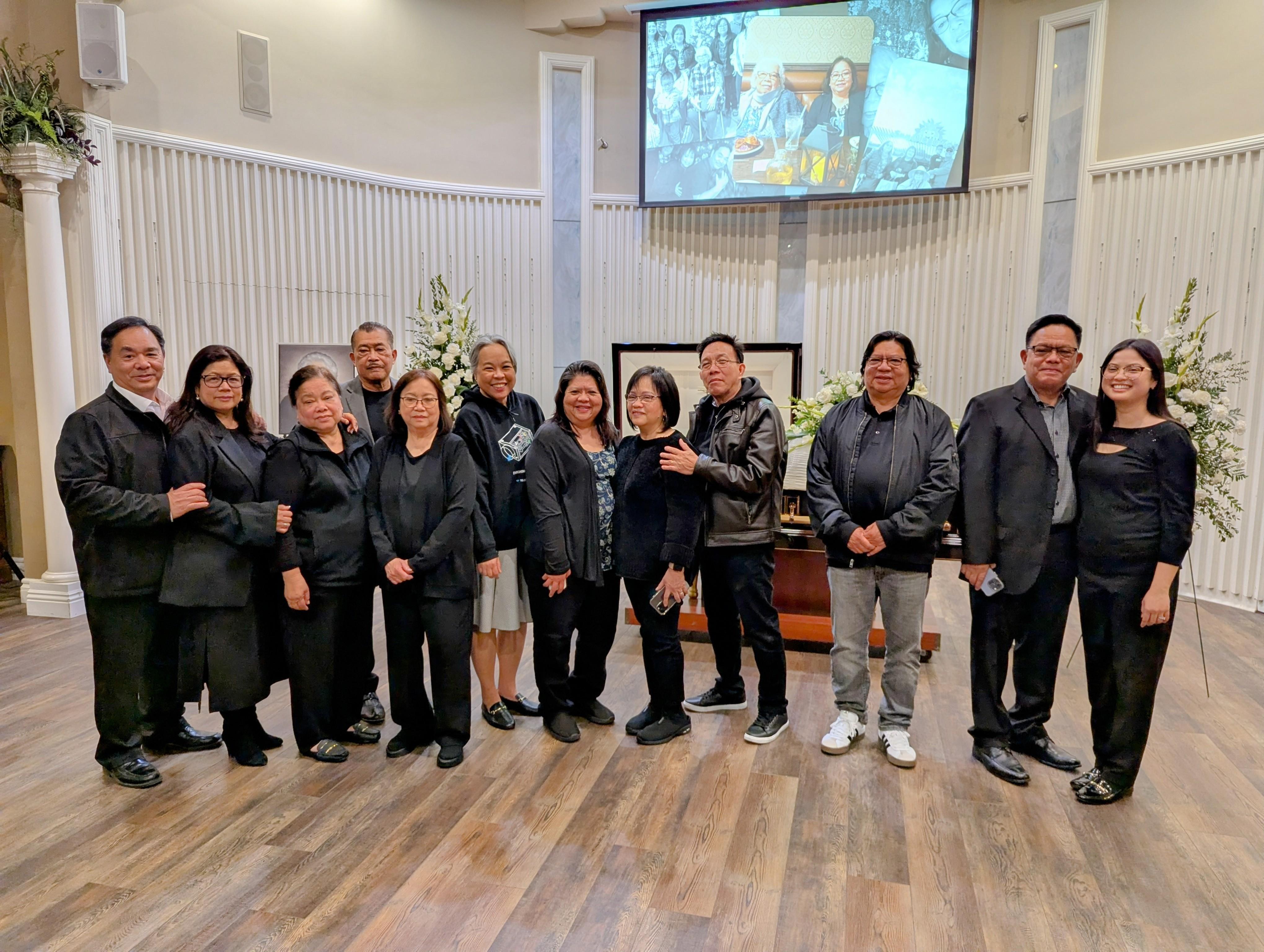 Family and friends in black gather at a memorial, sharing heartfelt moments.