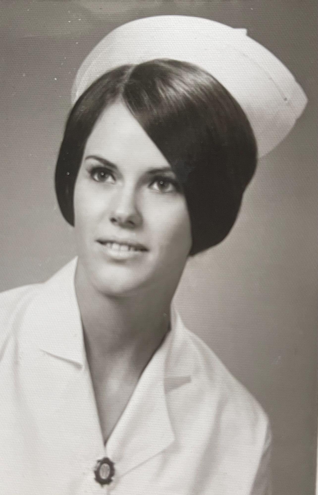 A young nurse is posed in a white uniform and cap, smiling confidently in a studio.
