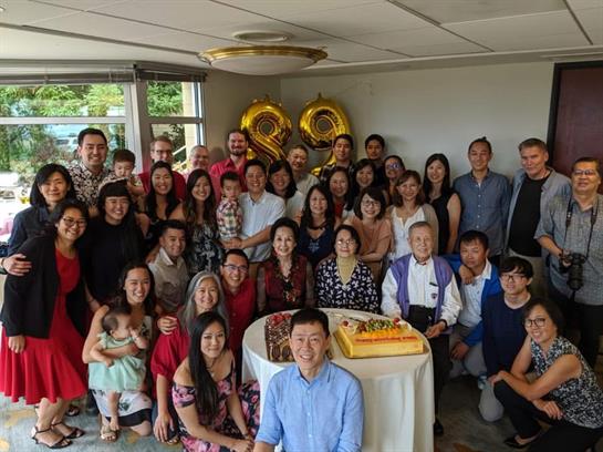 Groups of family and friends gather around a birthday cake, celebrating joyfully in a bright space.