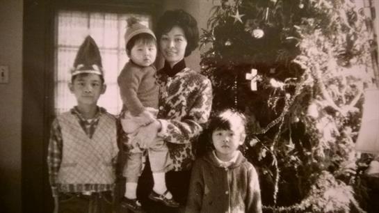 Four family members stand together in front of a decorated Christmas tree at home.