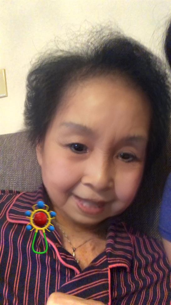 A young girl smiles joyfully while sitting indoors, wearing a vibrant patterned outfit.