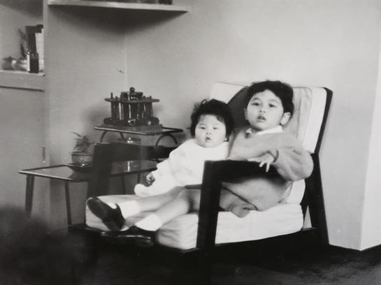Two young children are comfortably seated side by side in a chair, sharing a quiet moment.