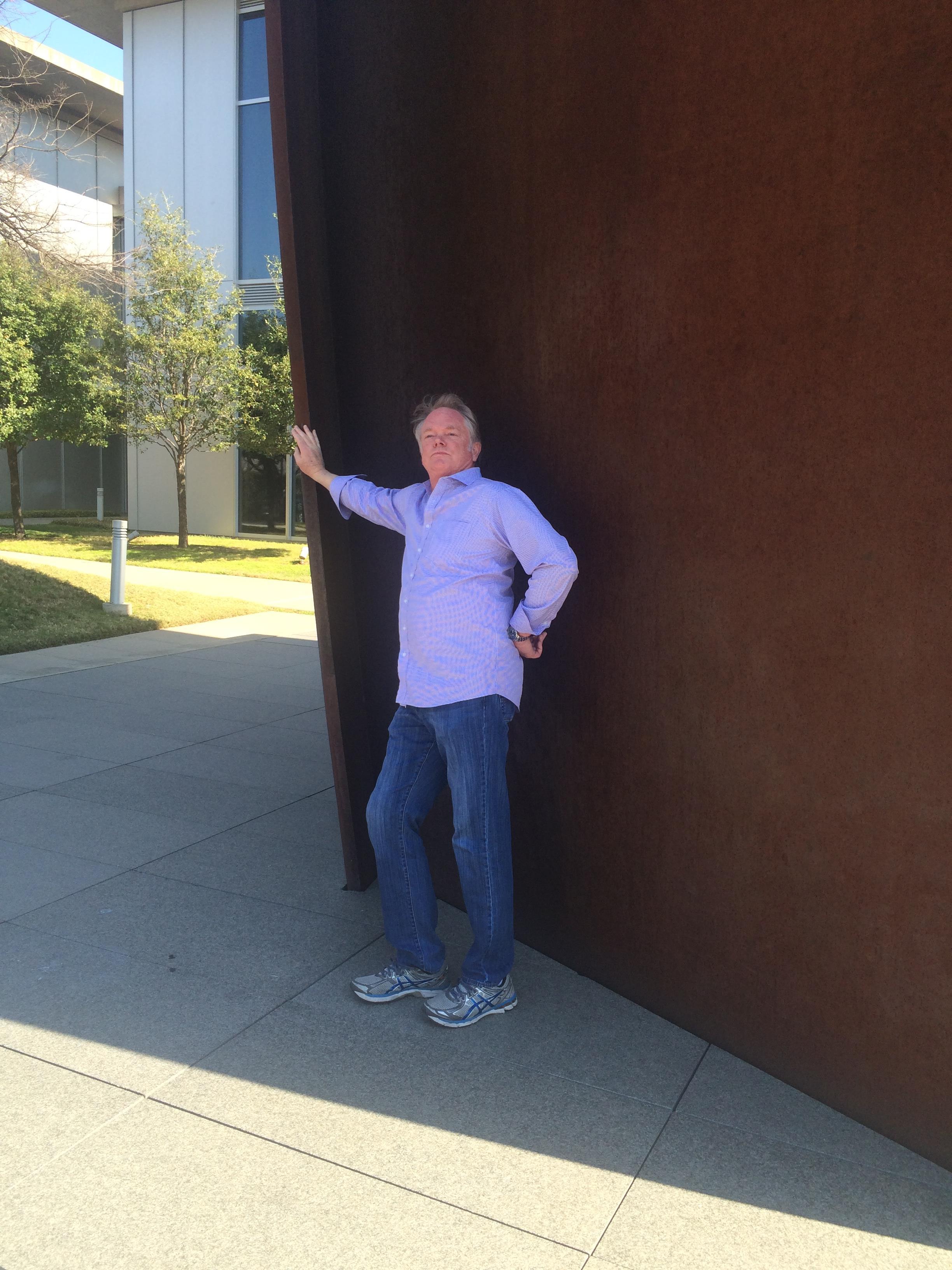 A man stands confidently by a large sculpture, enjoying the clear skies and open layout.