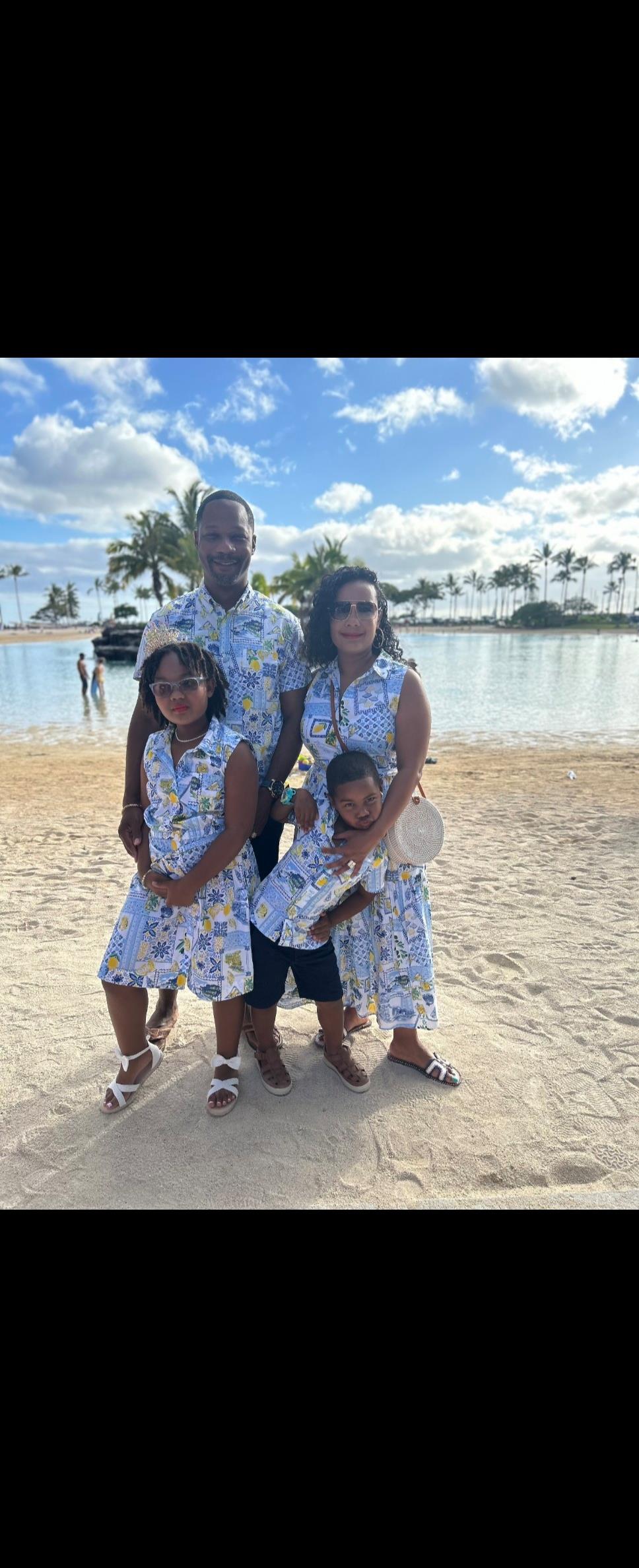 A cheerful family poses together at the beach by the water, surrounded by palm trees.