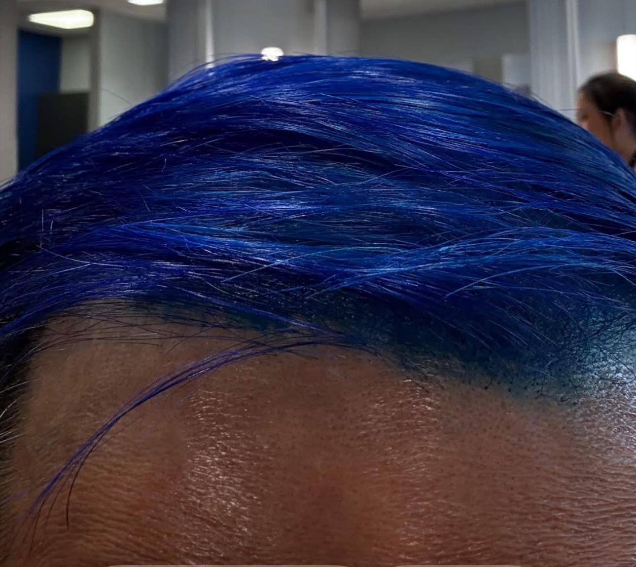 A client shows off their vibrant blue hair, styled in a contemporary salon filled with activity.