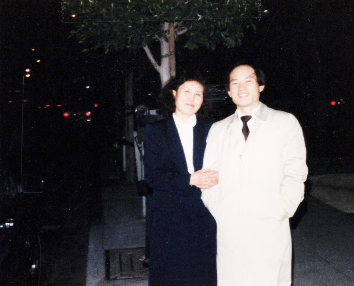 A couple enjoys a nighttime walk together in a city, dressed warmly and smiling.