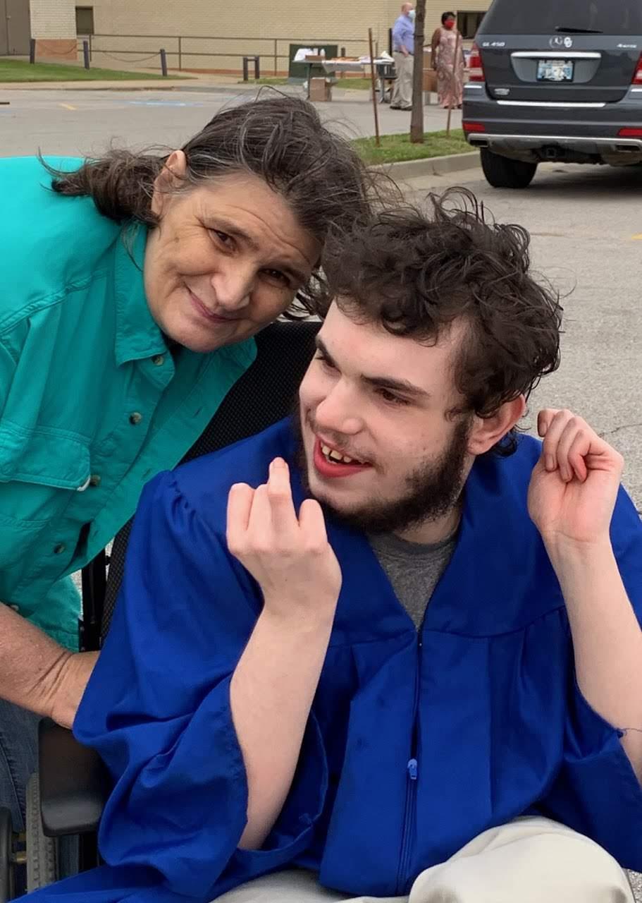 A caregiver and a young man share a lighthearted moment outside on a sunny day.