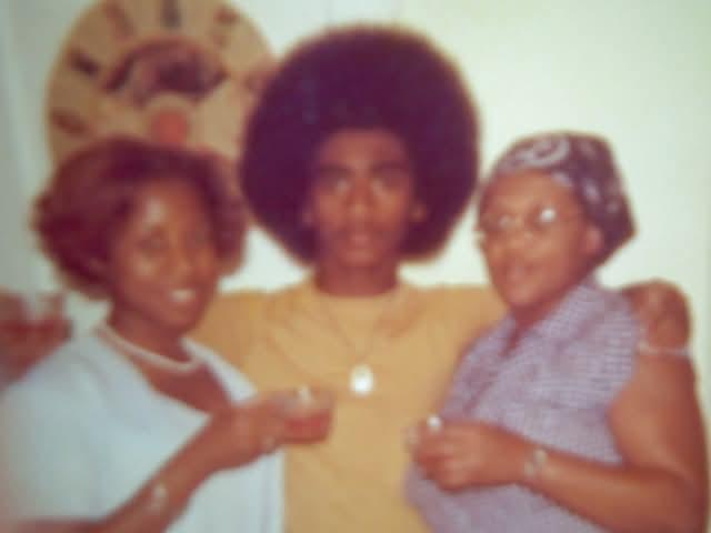 Three individuals gather in a cozy space, sharing drinks and smiles during a festive event.