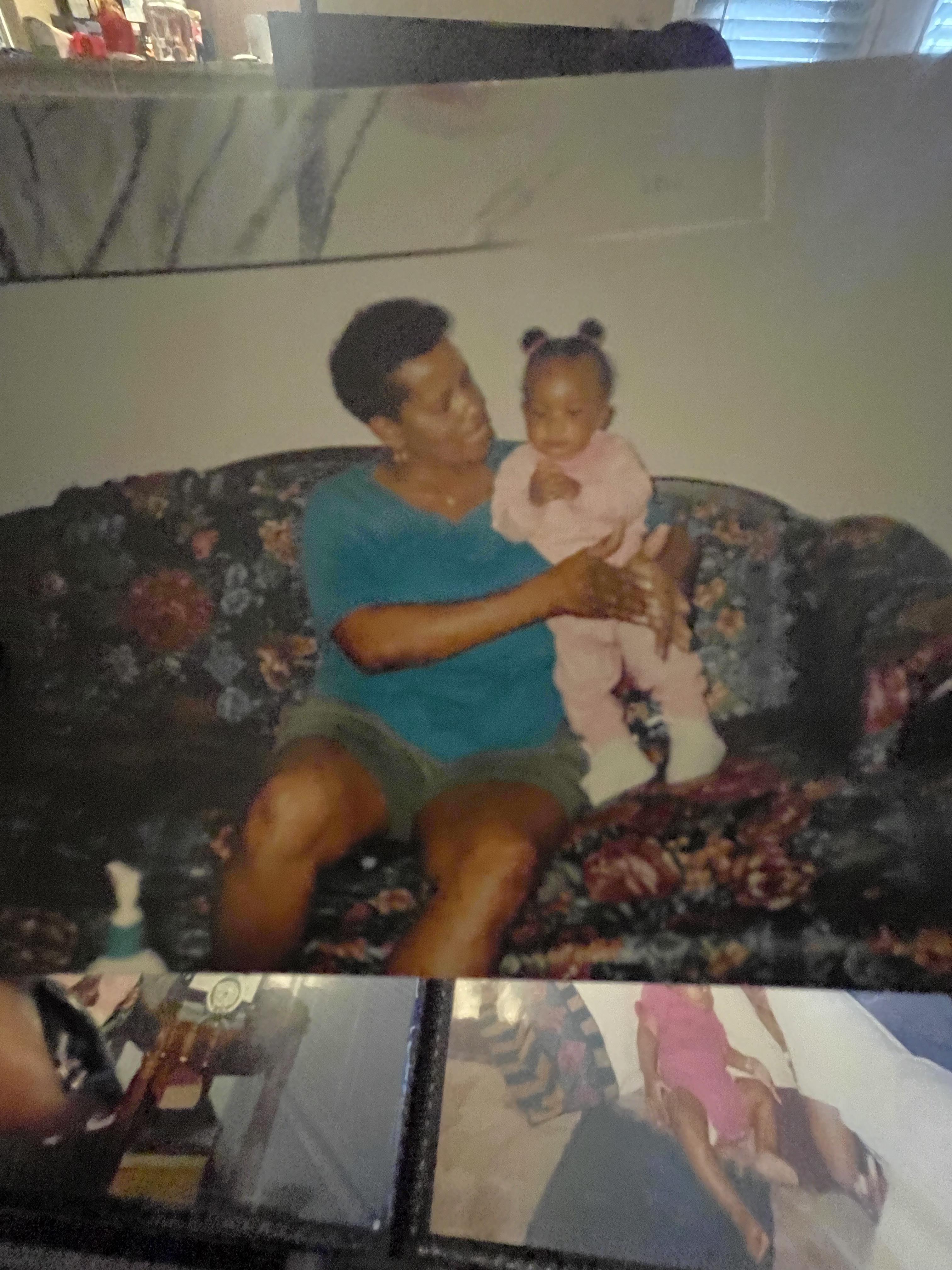A grandmother joyfully holds her grandchild on a floral patterned couch, sharing a tender moment.
