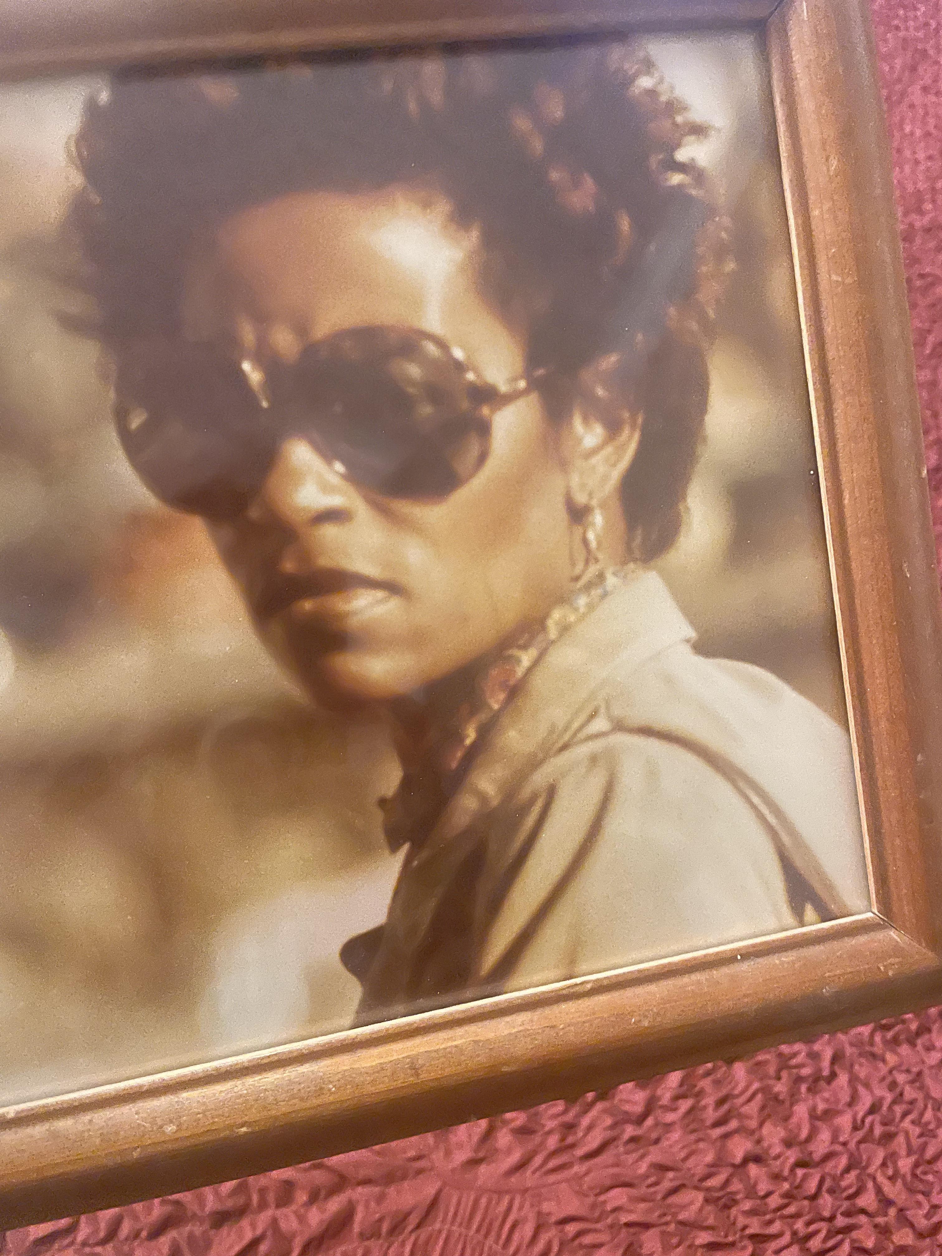 A confident woman with curly hair and sunglasses gazes at the viewer, exuding timeless style.