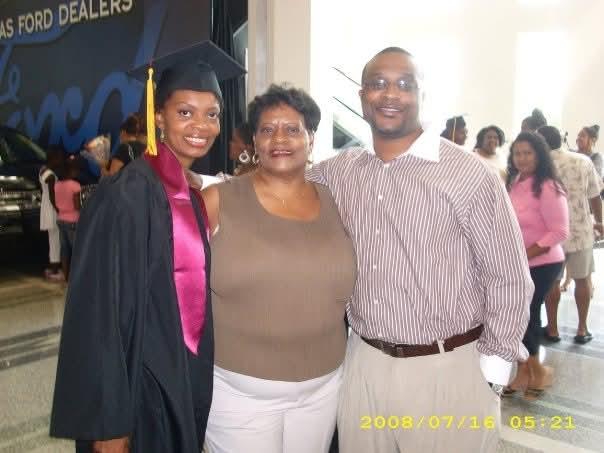 A graduate dressed in a cap and gown poses proudly with family members in the crowd.