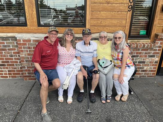 Five family members enjoy time together outside a restaurant during a sunny day.