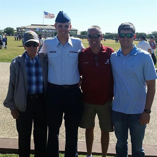 Four family members celebrate a graduation at a military ceremony under a clear blue sky.