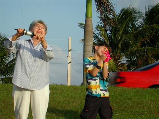 A lively interaction unfolds between a grandmother singing and her playful grandson in a sunny park.