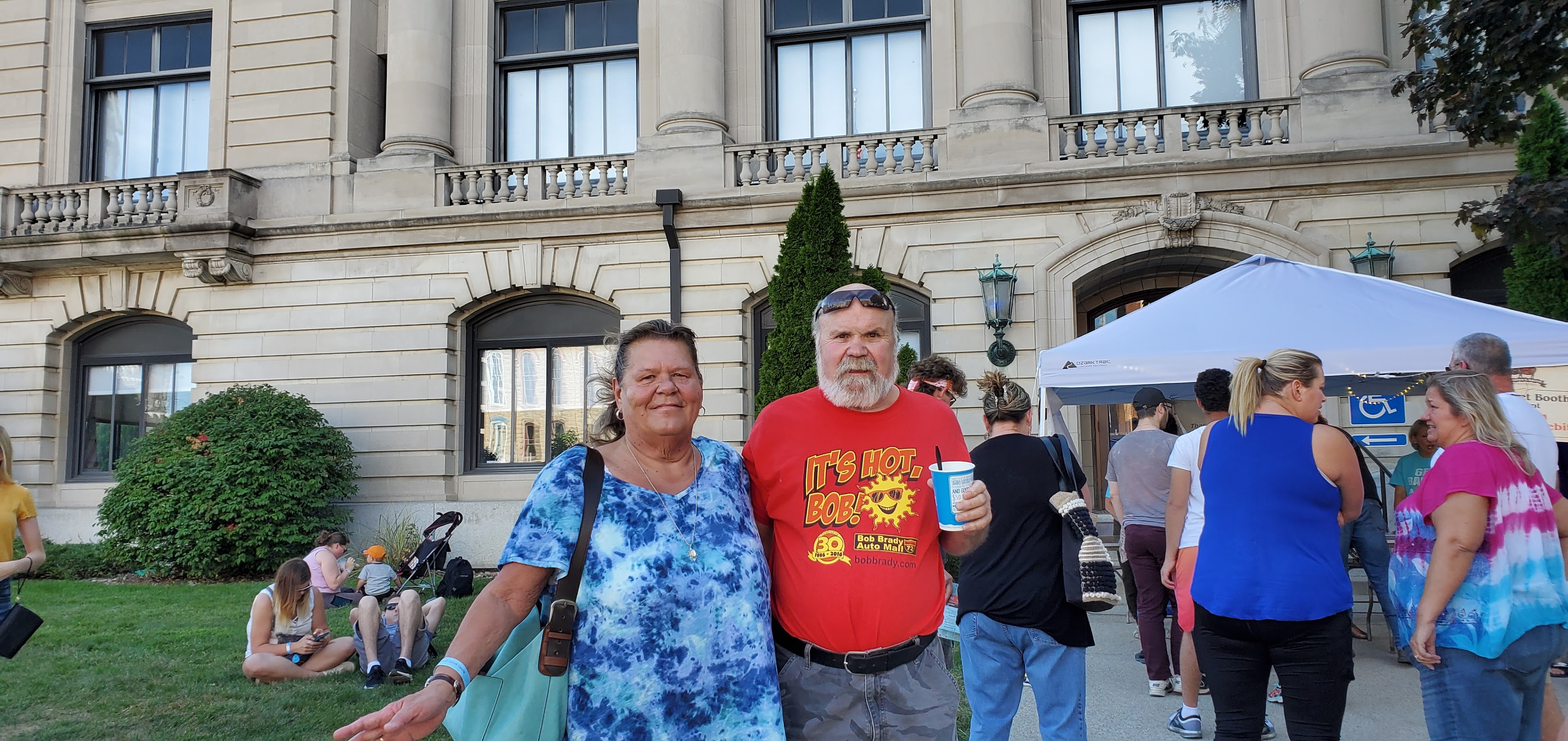 A couple smiles and poses for a picture at an event outside a large building.