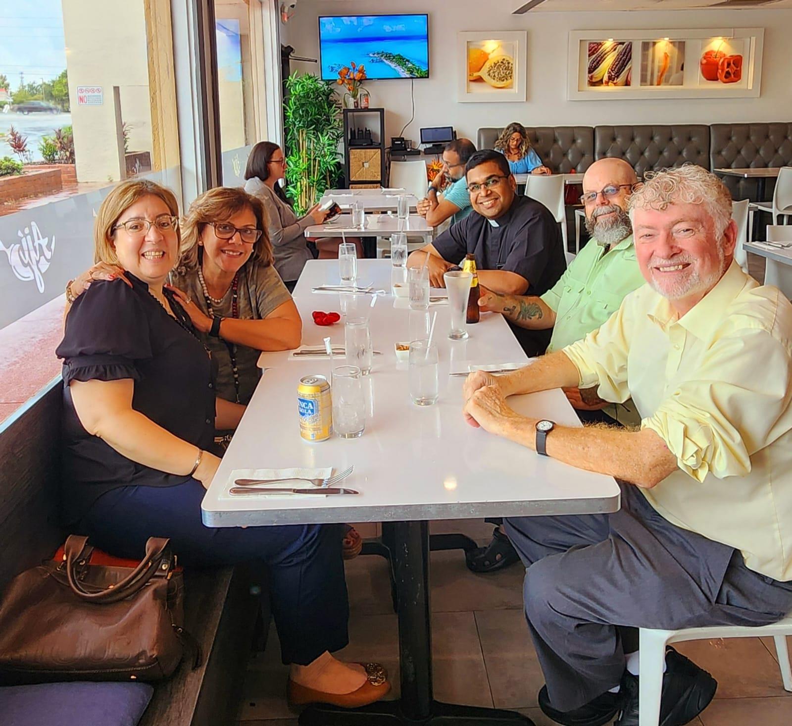 Group of friends sit together at a table, sharing laughter and drinks in a sunny restaurant.