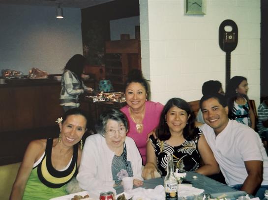 Group of five people smiling and enjoying a festive meal together in a lively restaurant setting.