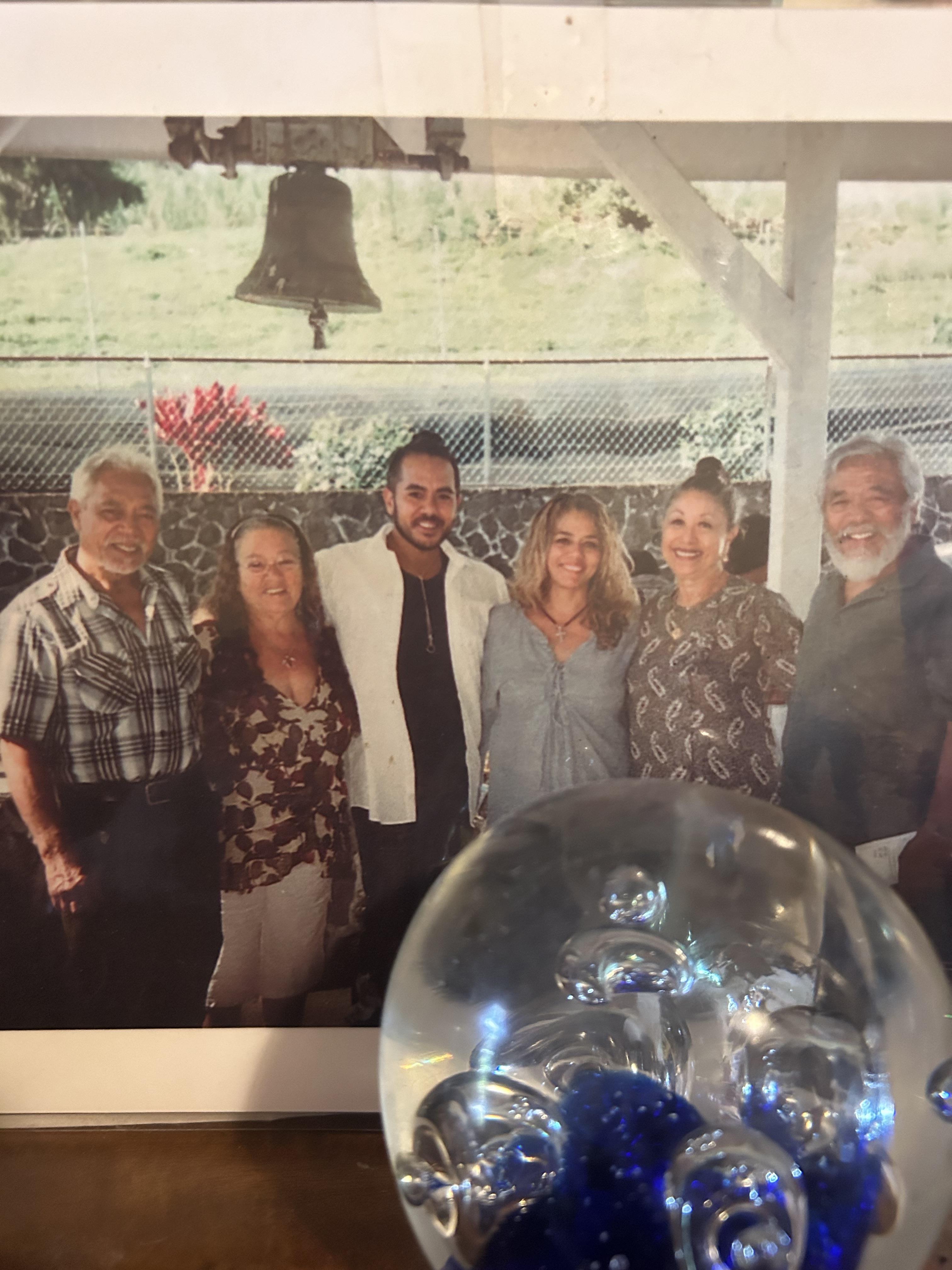 A group of six family members poses together outdoors near a large bell, sharing smiles.