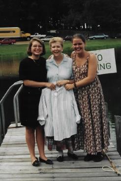A joyful moment captures three women posing on a dock beside a quiet lake.