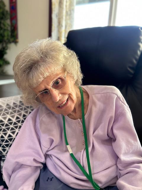An elderly woman with silver hair happily relaxes in a cozy chair, enjoying her surroundings.