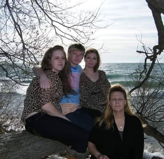 Four friends sit on a branch, enjoying a calm day by the ocean with gentle waves.