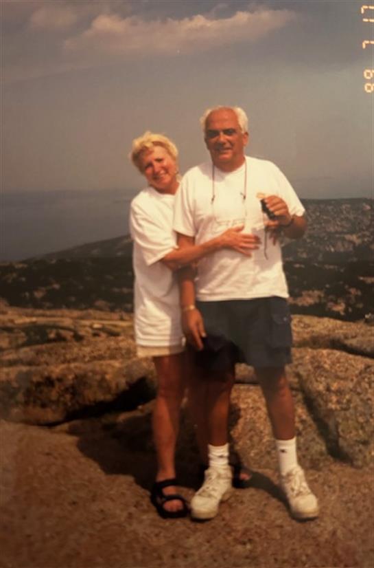 A happy couple poses for a picture atop a mountain, enjoying the sunny weather and scenic views.