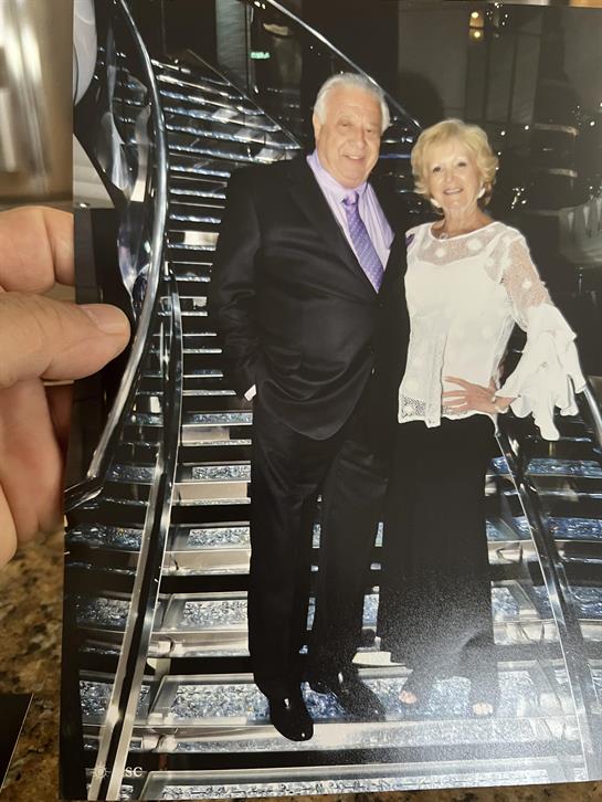 A well-dressed couple smiling as they stand together on a modern staircase, enjoying their evening.