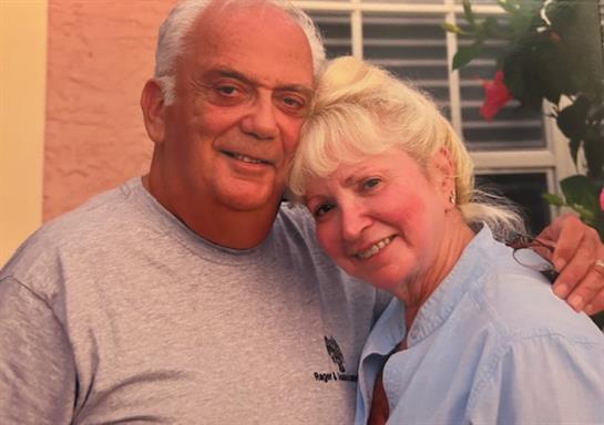Older couple smiles happily while embracing in their vibrant garden filled with flowers.