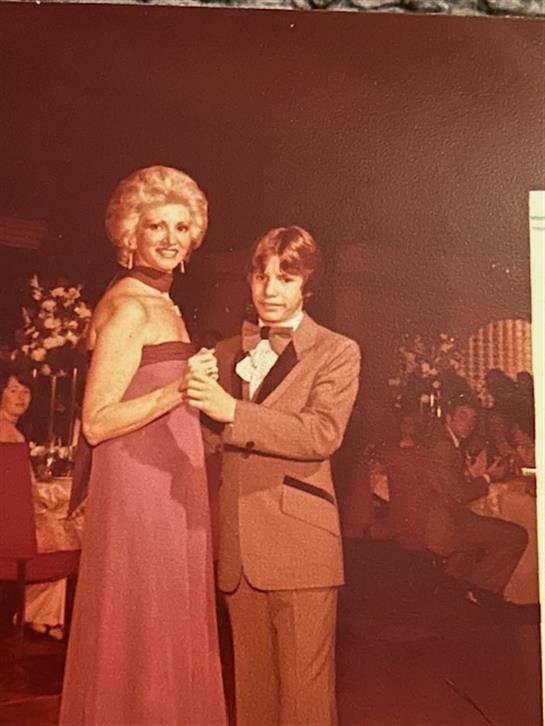 A young man and a glamorous woman dance together at a formal gathering in an upscale venue.