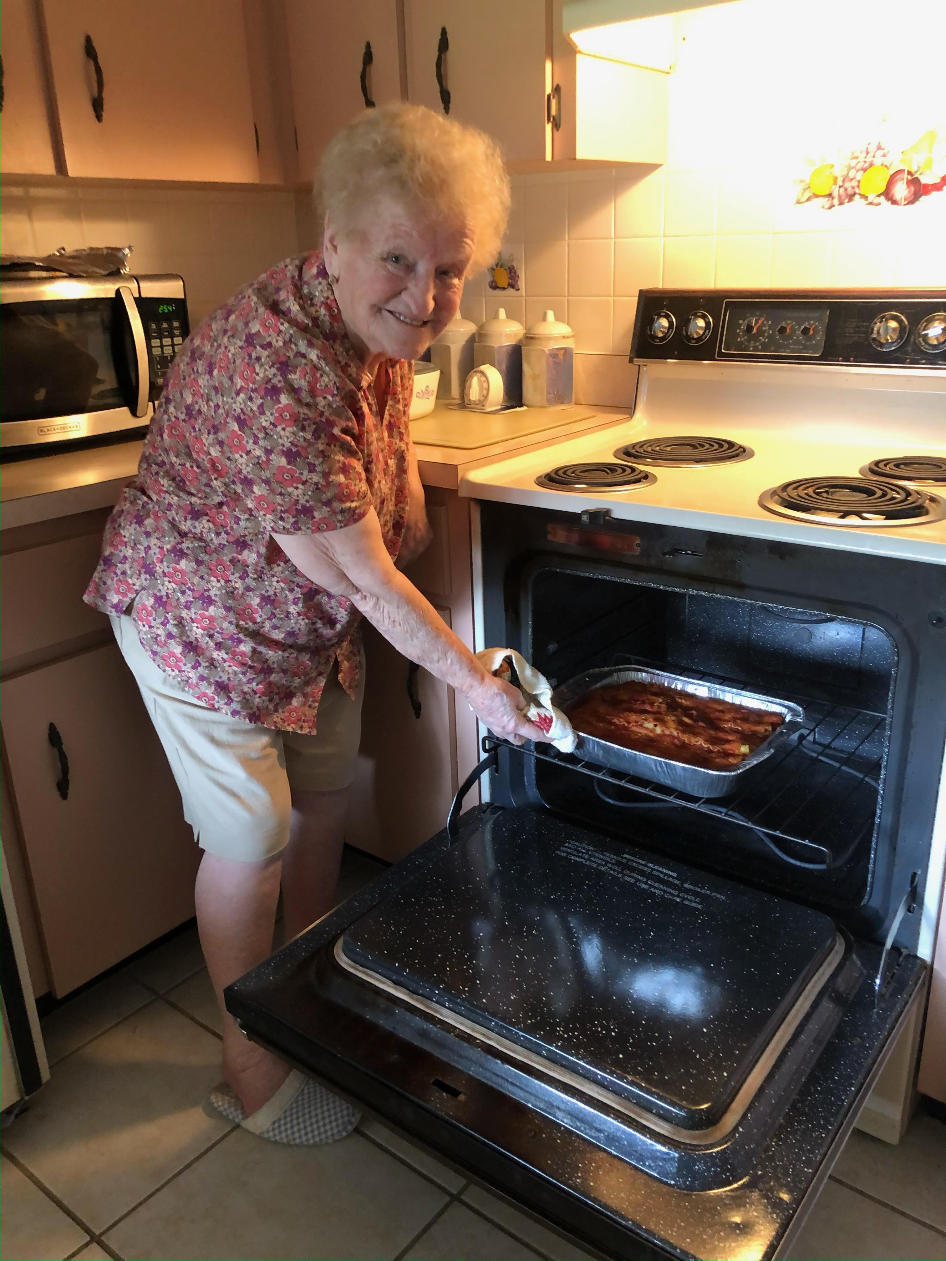 A cheerful elderly woman removes a casserole from the oven in her warm kitchen.