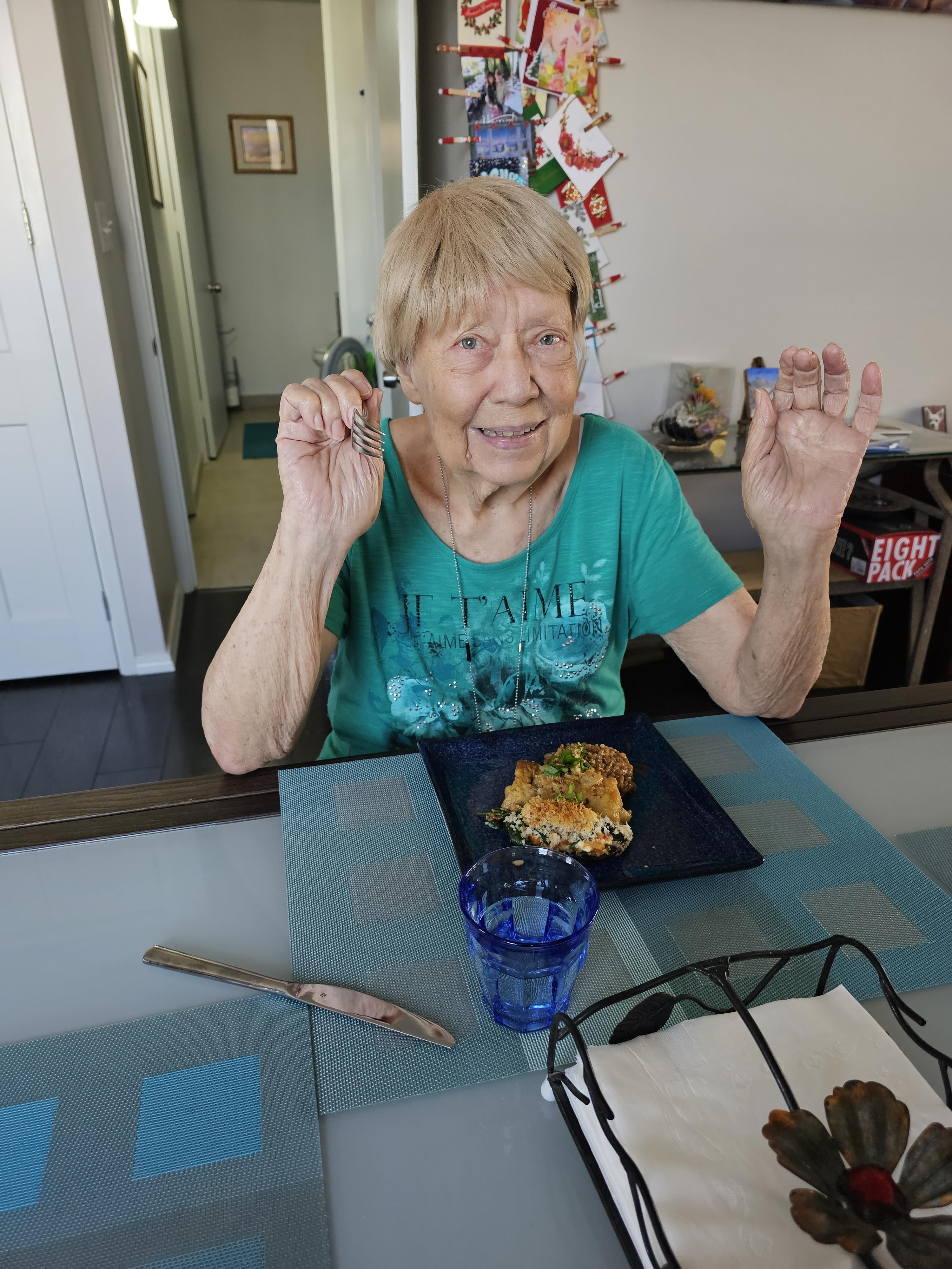 Woman in a green shirt smiles while enjoying her food in a cheerful indoor environment.