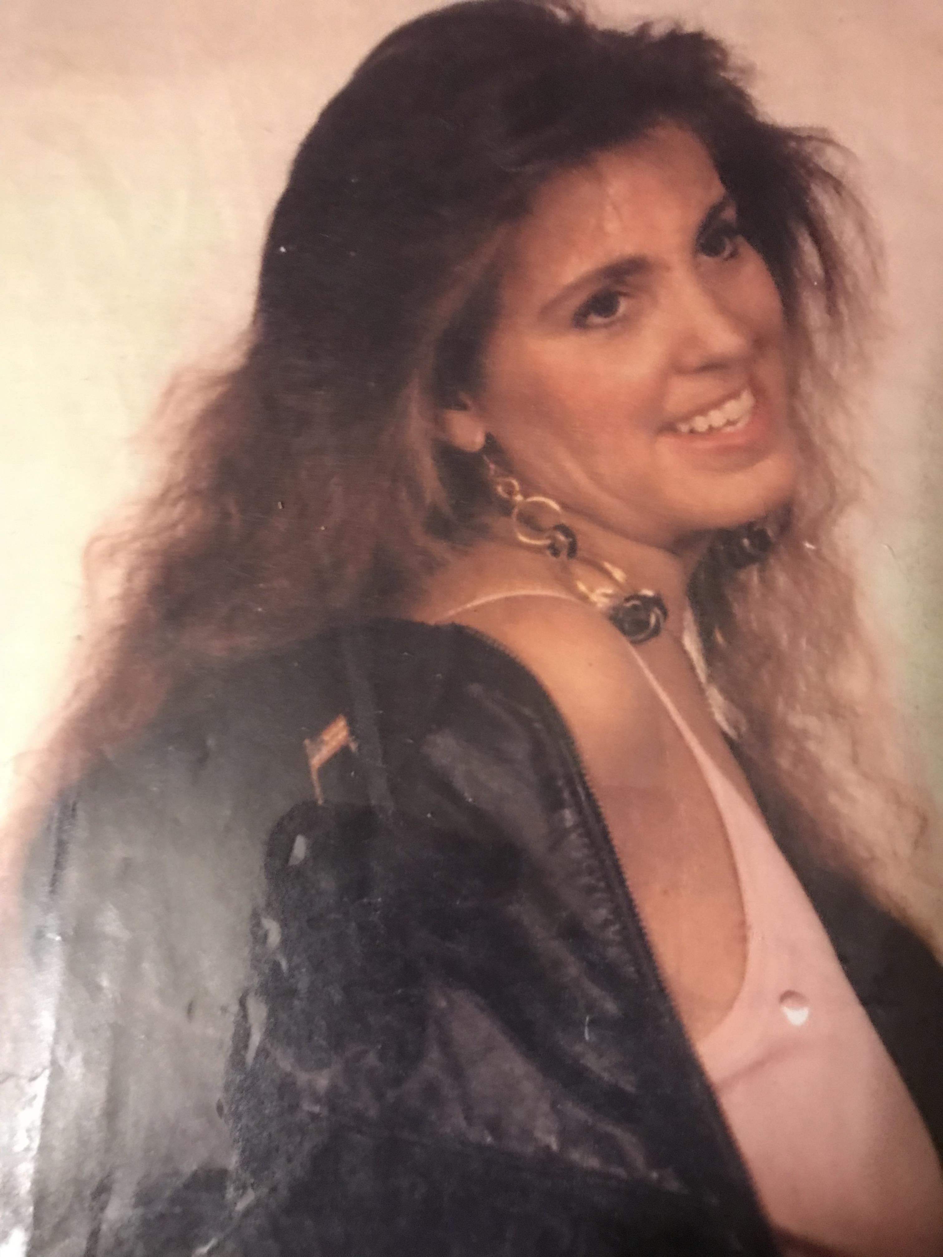 A woman smiles while wearing a fashionable outfit and large earrings, showcasing her style.