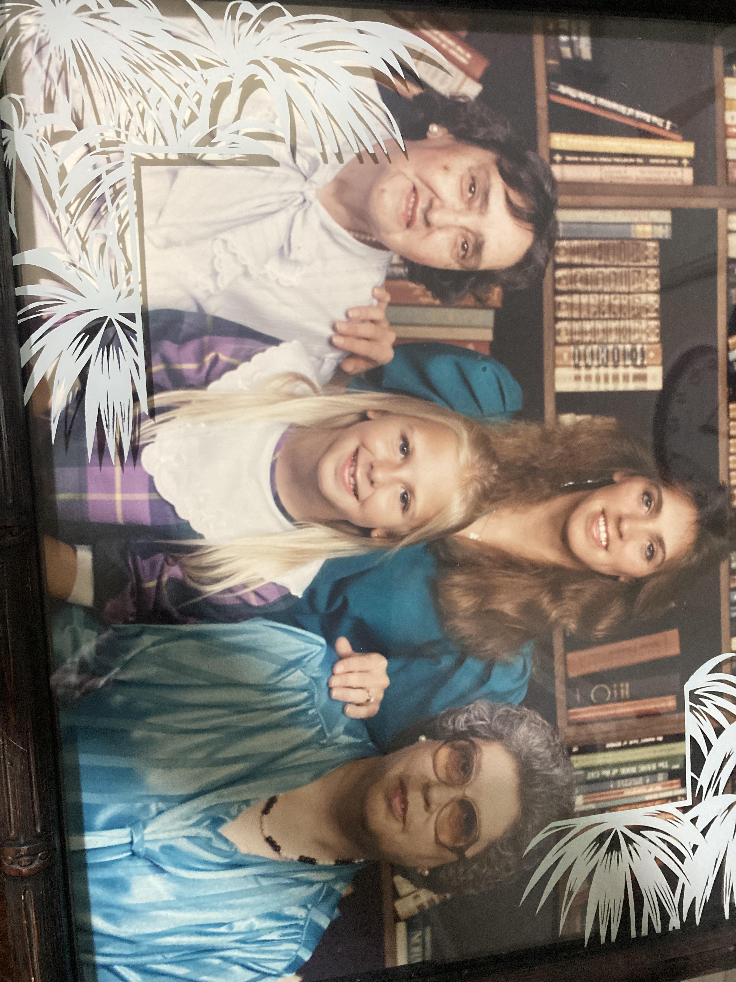 Four women of different ages pose together in a cozy library while smiling warmly.