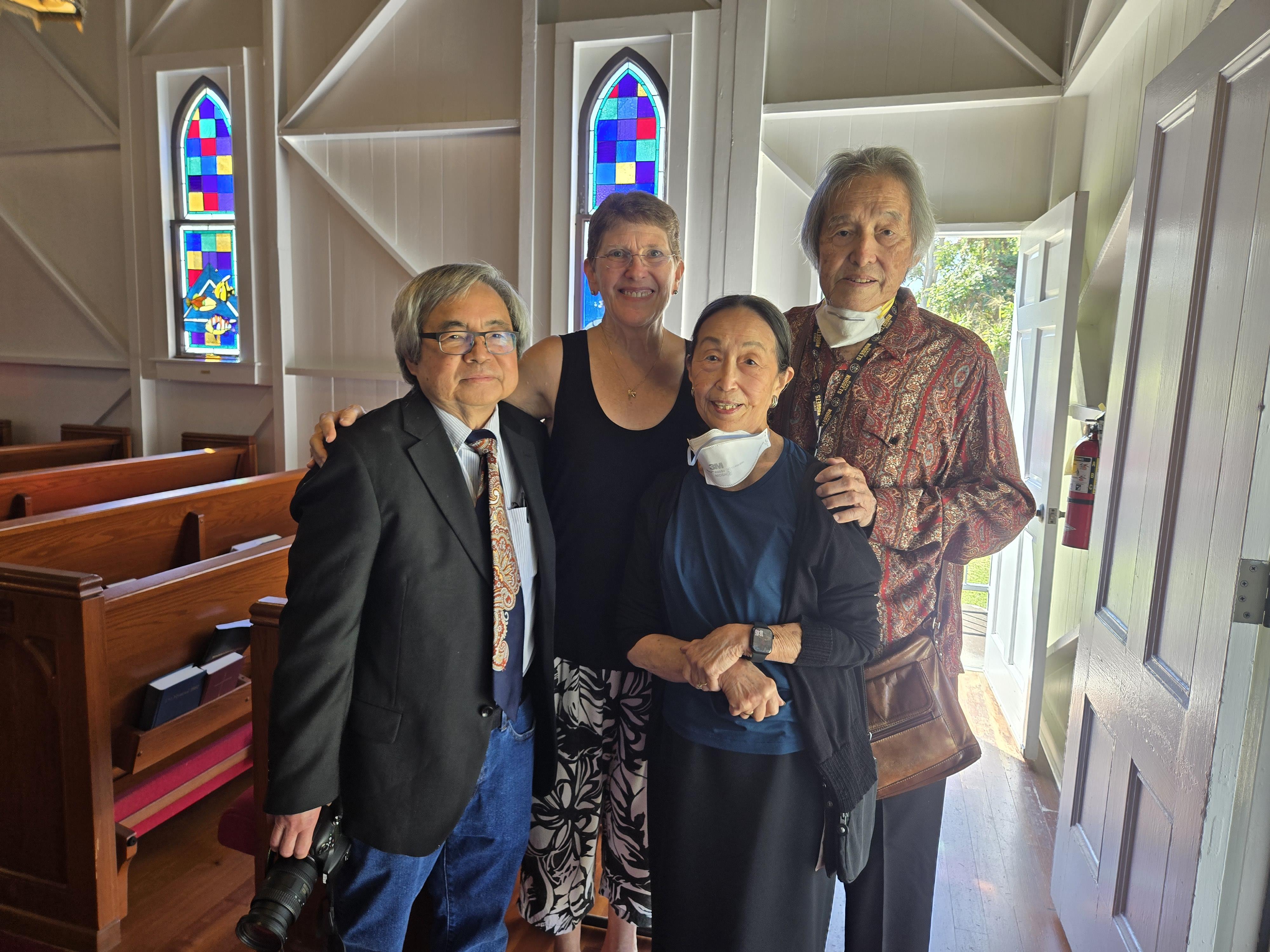 Four people joyfully pose together inside a chapel with colorful stained glass windows.